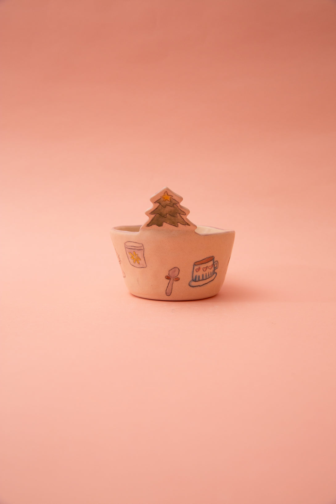 Small ceramic bowl with a christmas tree design on a pink background