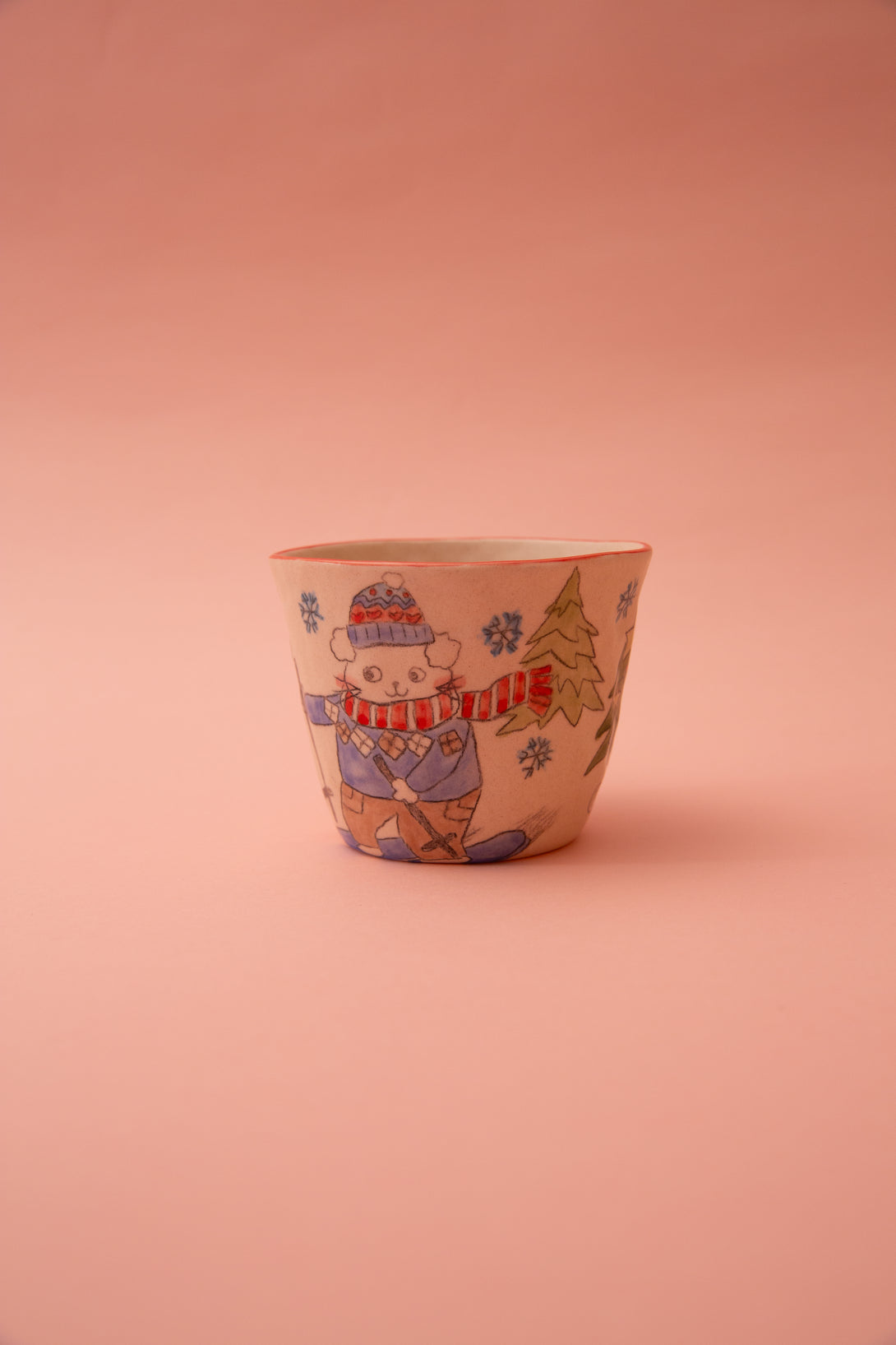 Ceramic cup with a winter-themed design of a cat in a hat and scarf on a pink background