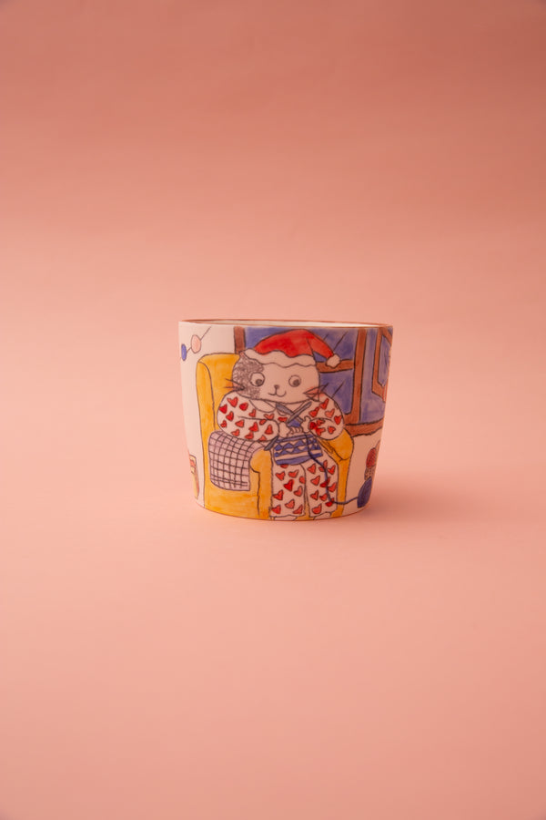 Ceramic mug with a colorful design of a character wearing a santa hat in a chair on a pink background