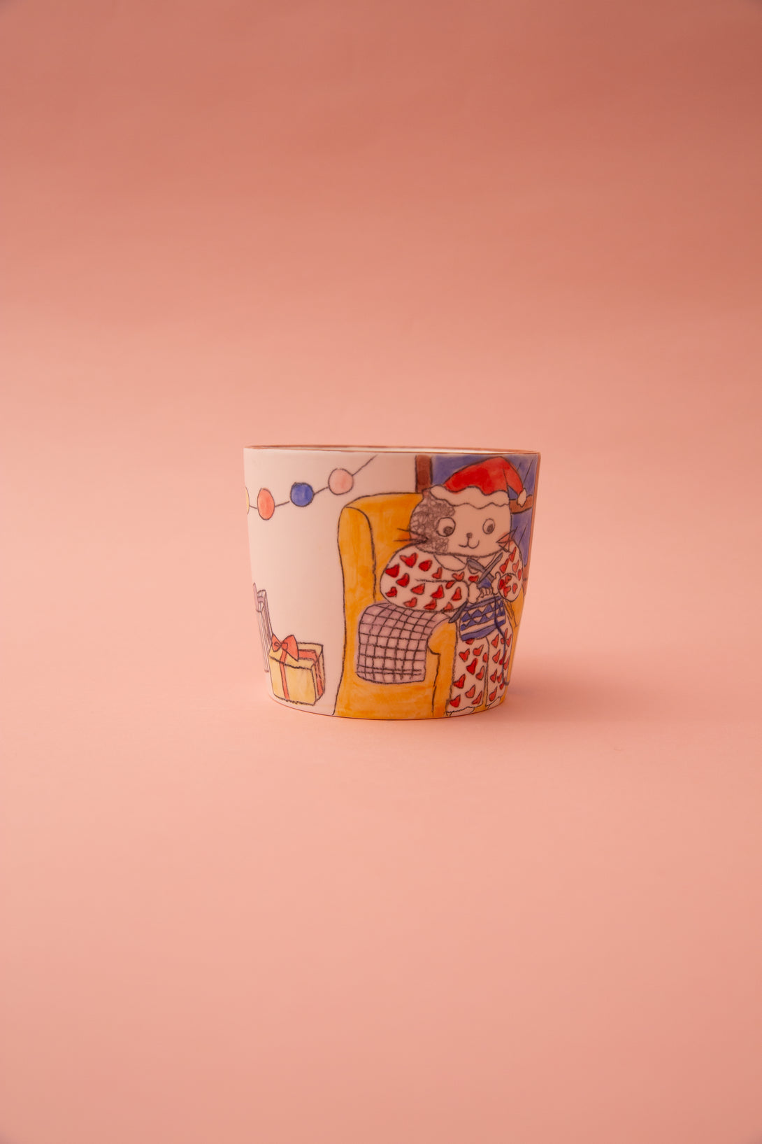 Ceramic mug with a cartoon design of a cat sitting on an armchair on a pink background