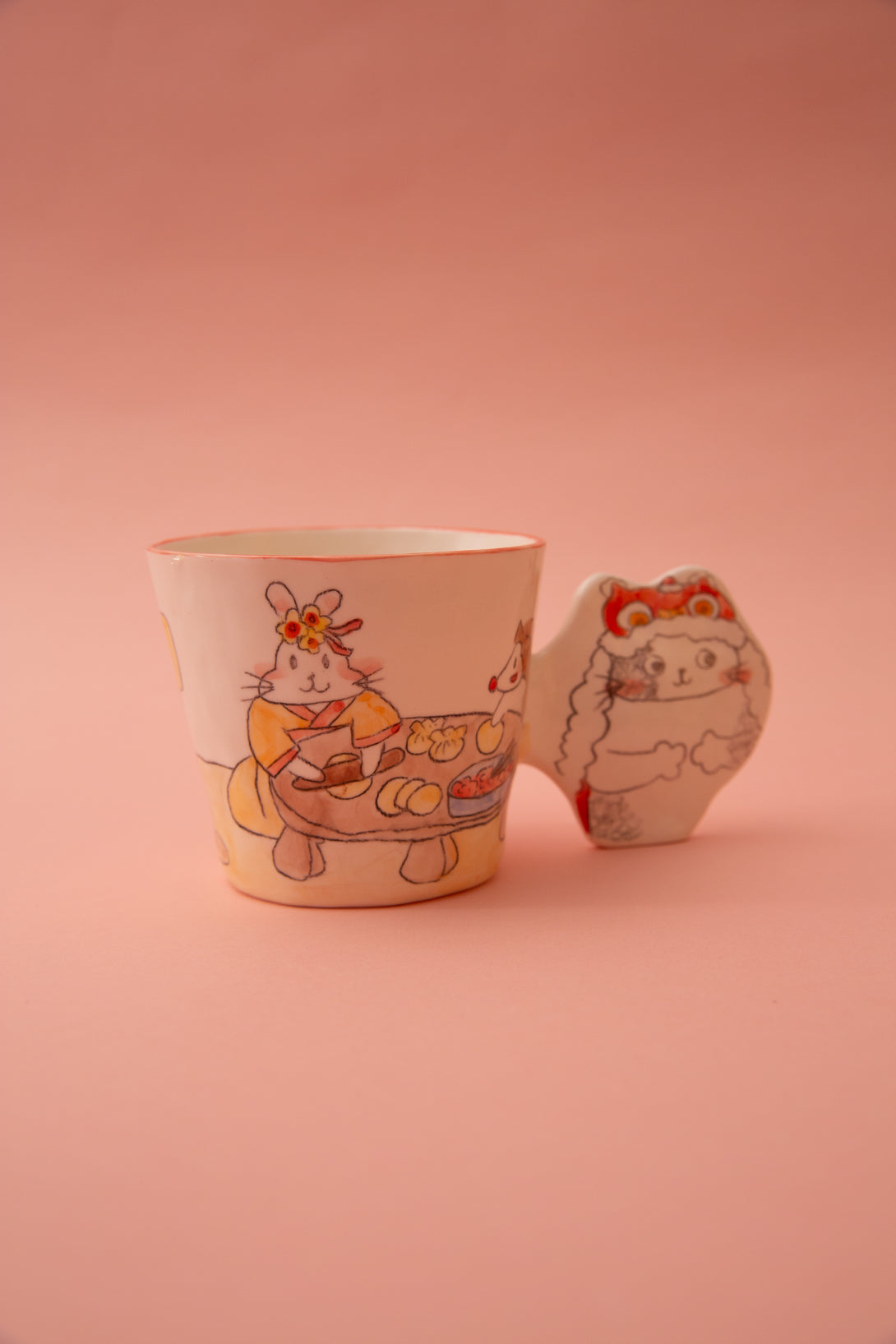 A ceramic mug with animal illustrations and a fun handle on a pink background