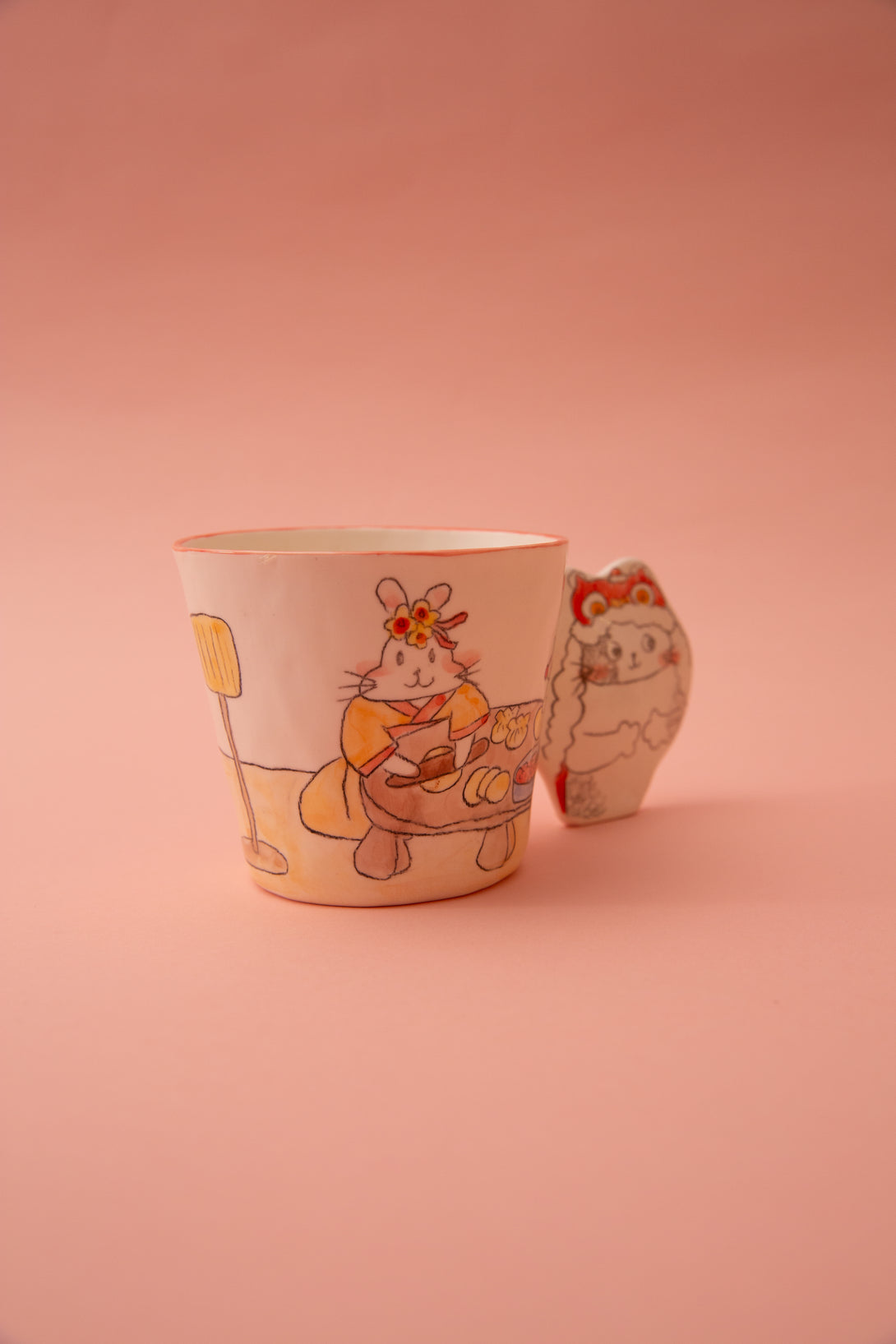 A ceramic mug with animal illustrations and a fun handle on a pink background