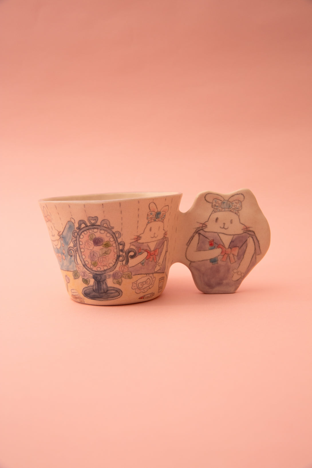 Ceramic cup with artistic designs and a fun handle on a pink background