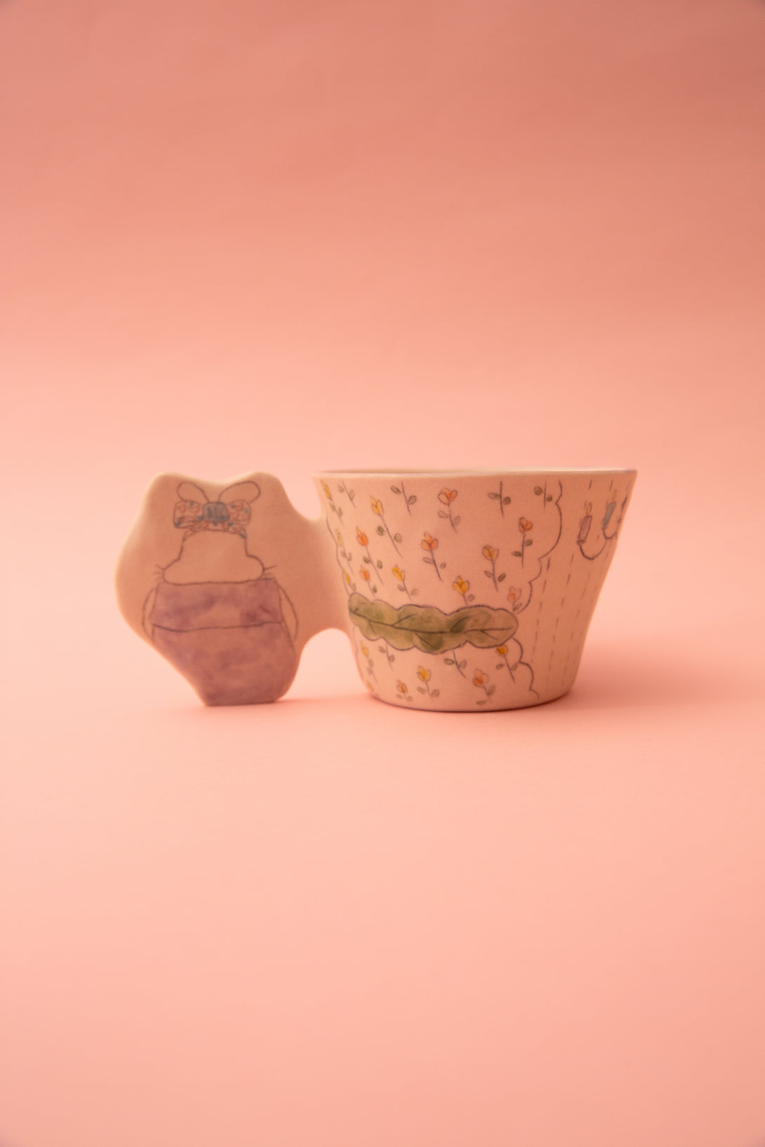 A ceramic mug with floral patterns and an irregularly shaped handle on a pink background
