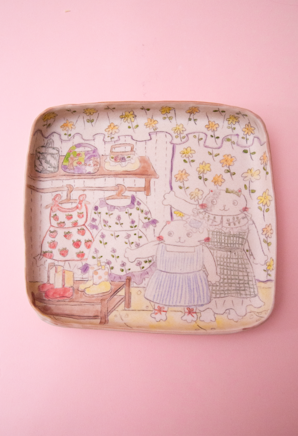 Plate with illustrated design of cartoon cat characters in a garden on a pink background