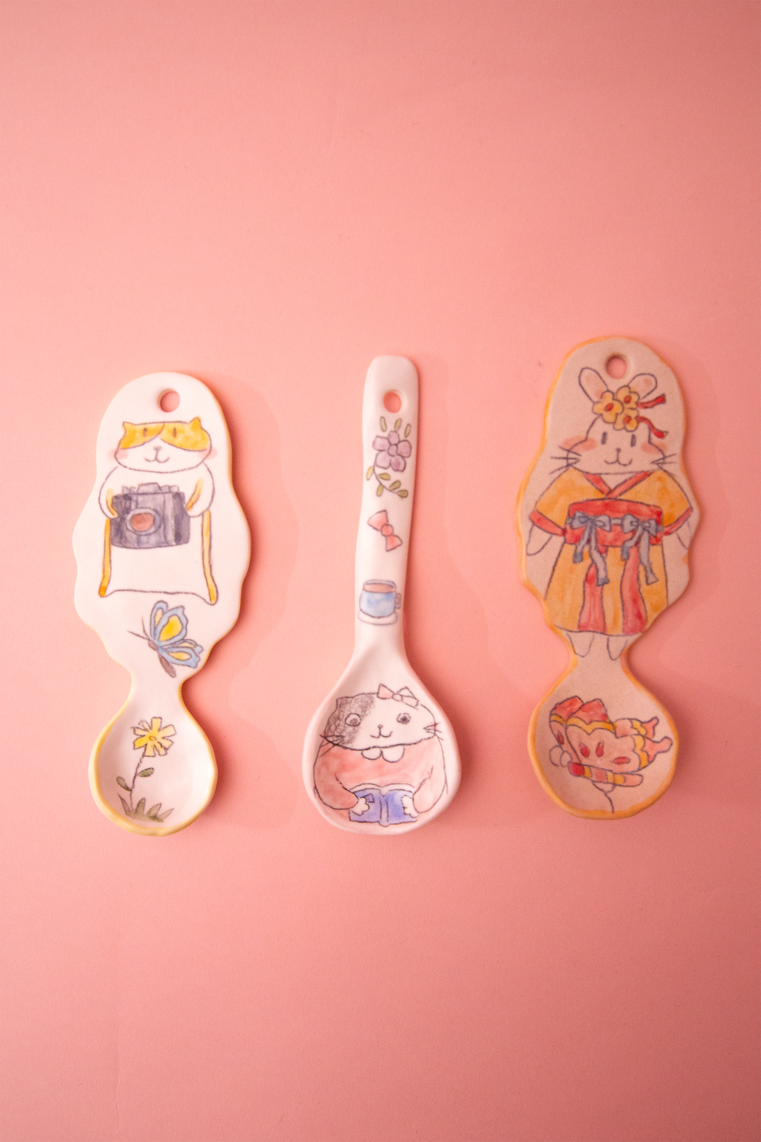 Three spoons with cartoon designs on a pink background