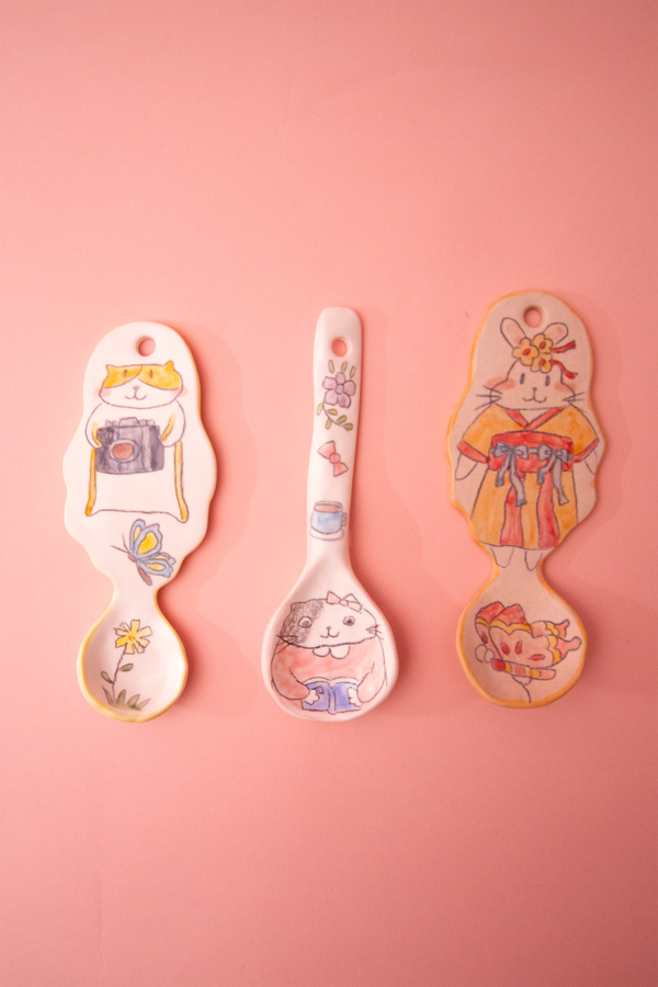 Three spoons with cartoon designs on a pink background