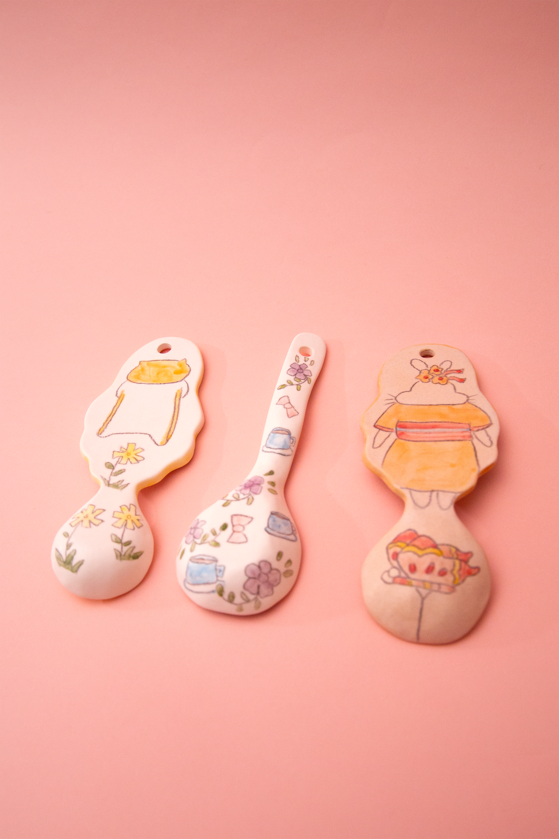 Three spoons with cartoon designs on a pink background