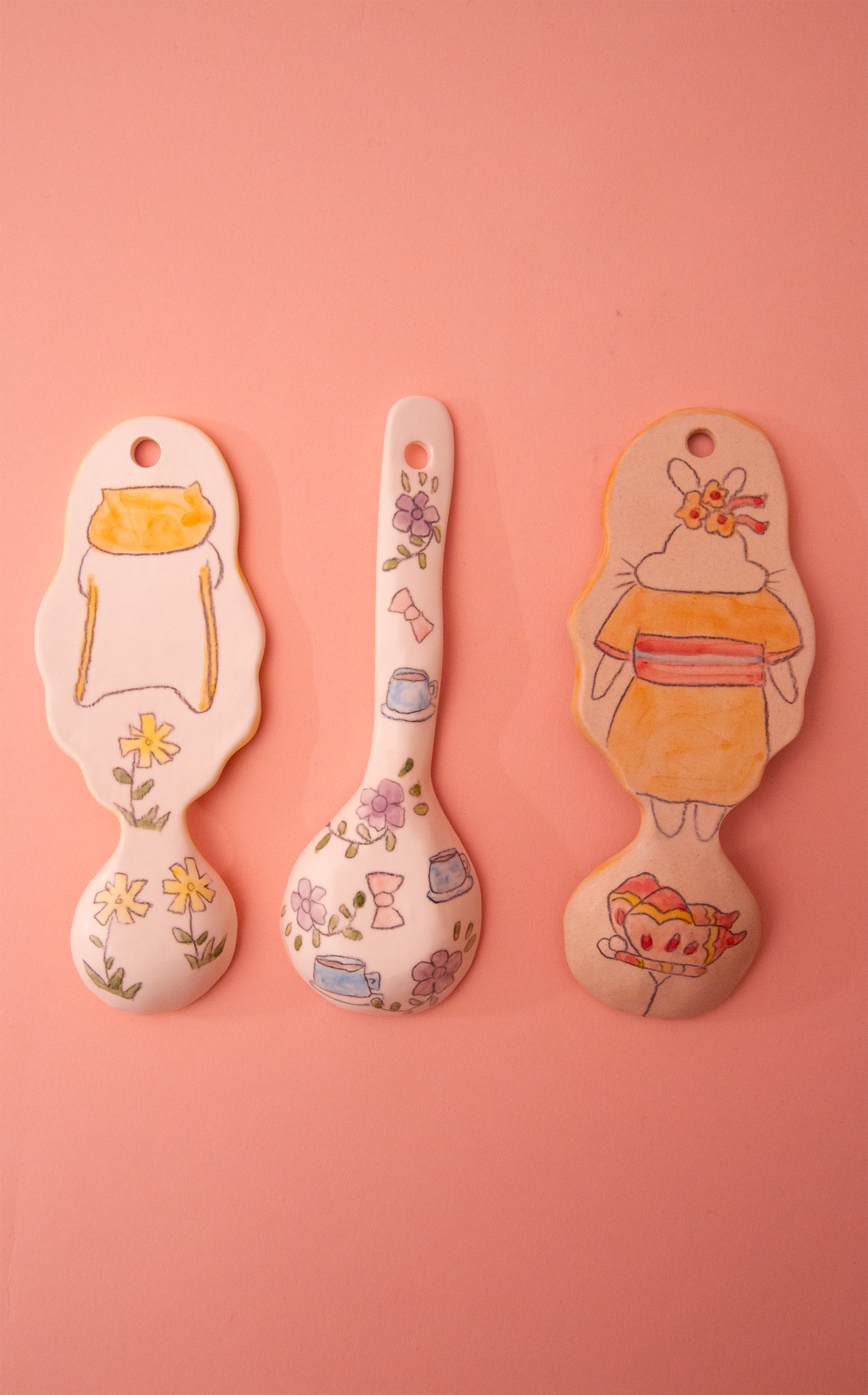 Three spoons with cartoon designs on a pink background