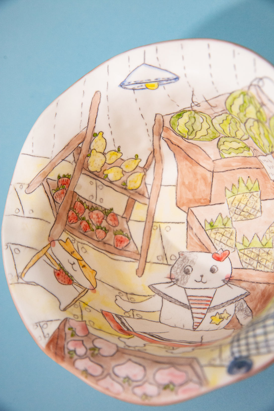 Illustrated bowl with a cat, flowers, and fruits on a blue background