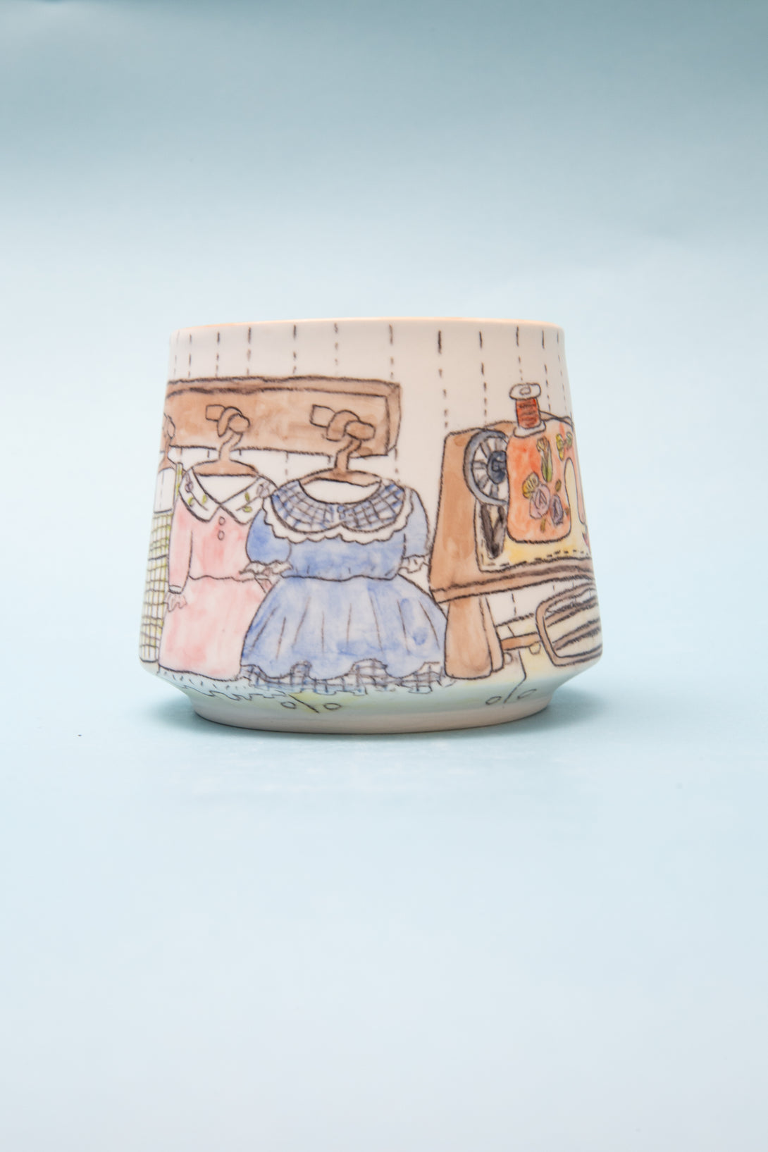 Ceramic mug with illustrations of a dress, coat, and hat on a light blue background
