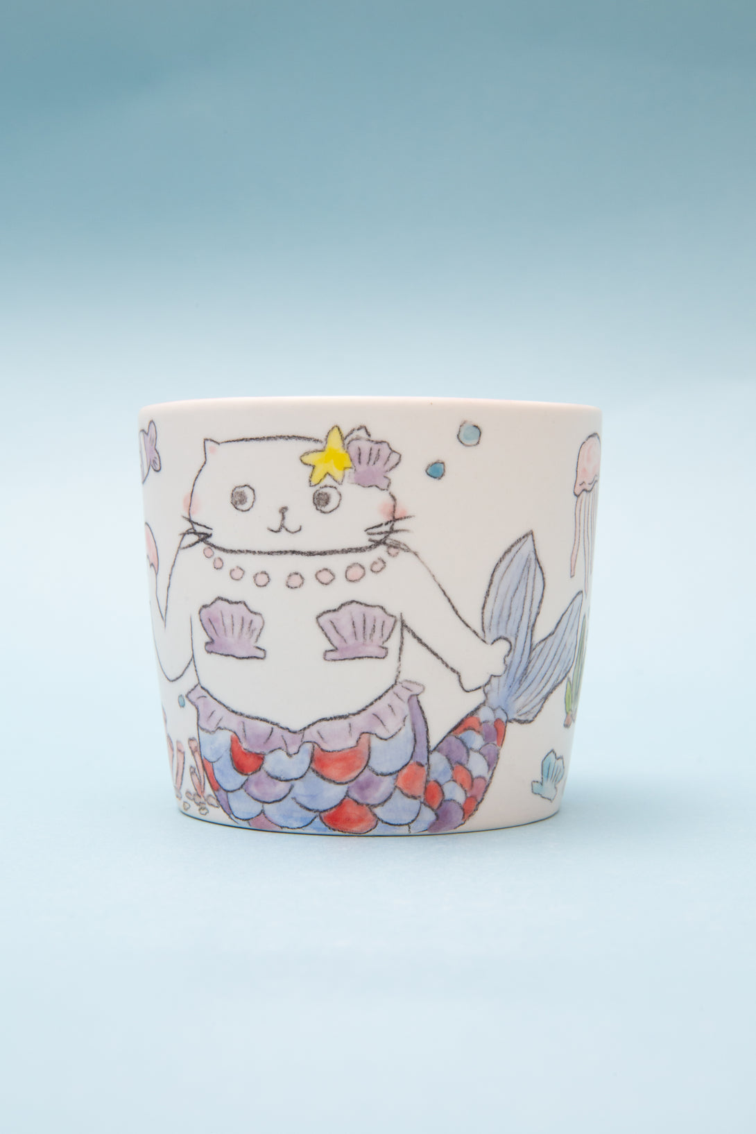 Ceramic mug with a cat mermaid design on a light blue background