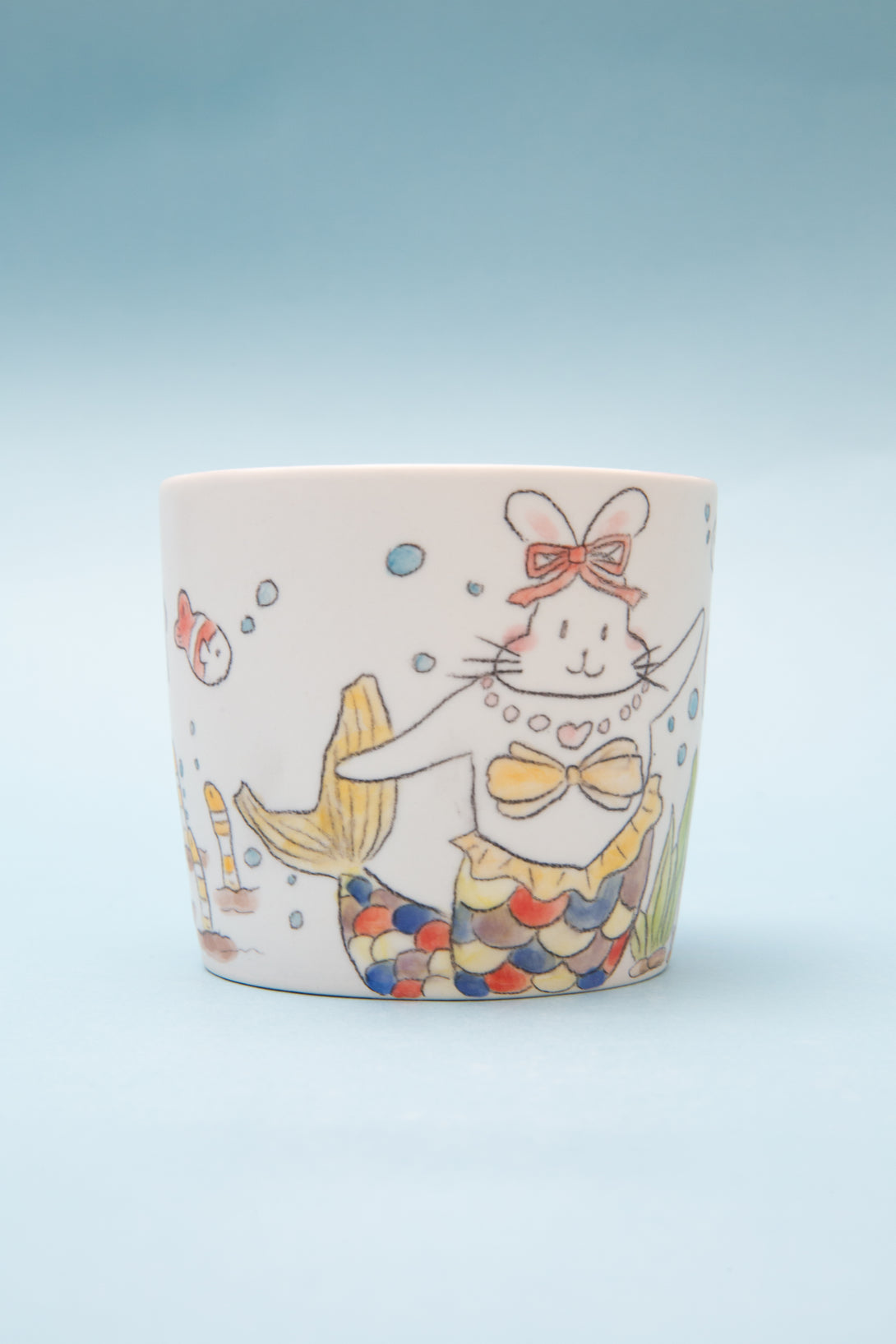 Ceramic mug with a colorful mermaid design on a light blue background