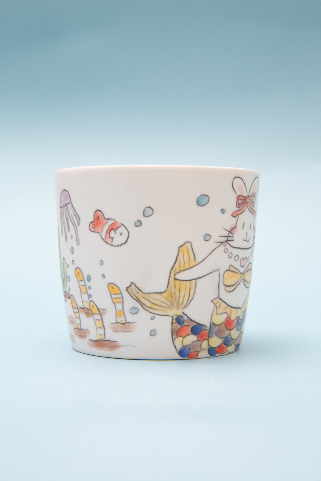 Ceramic mug with colorful cat illustration on a light blue background