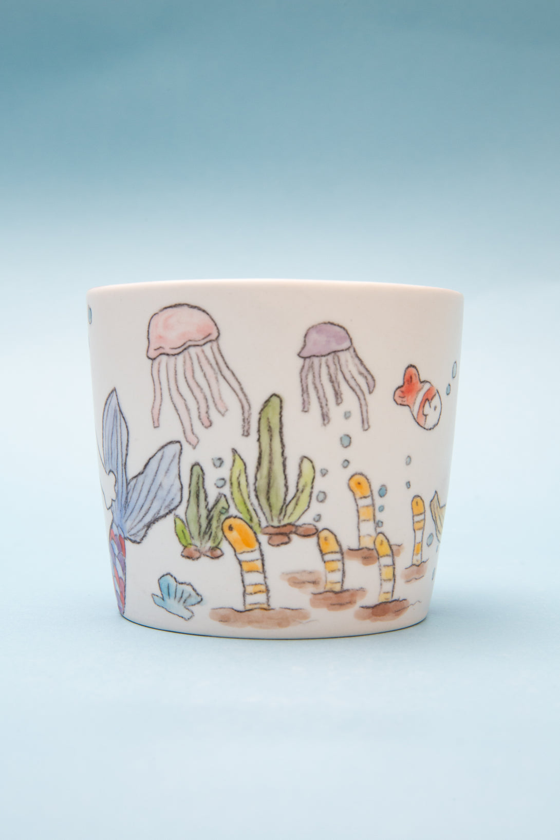 Ceramic mug with underwater scene illustrations on a light blue background