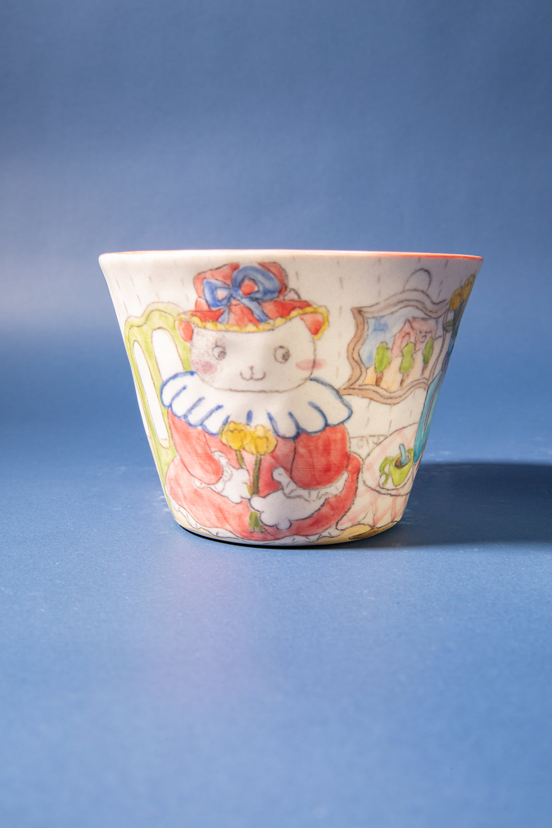 Ceramic cup with a colorful design of a cat wearing a hat on a blue background