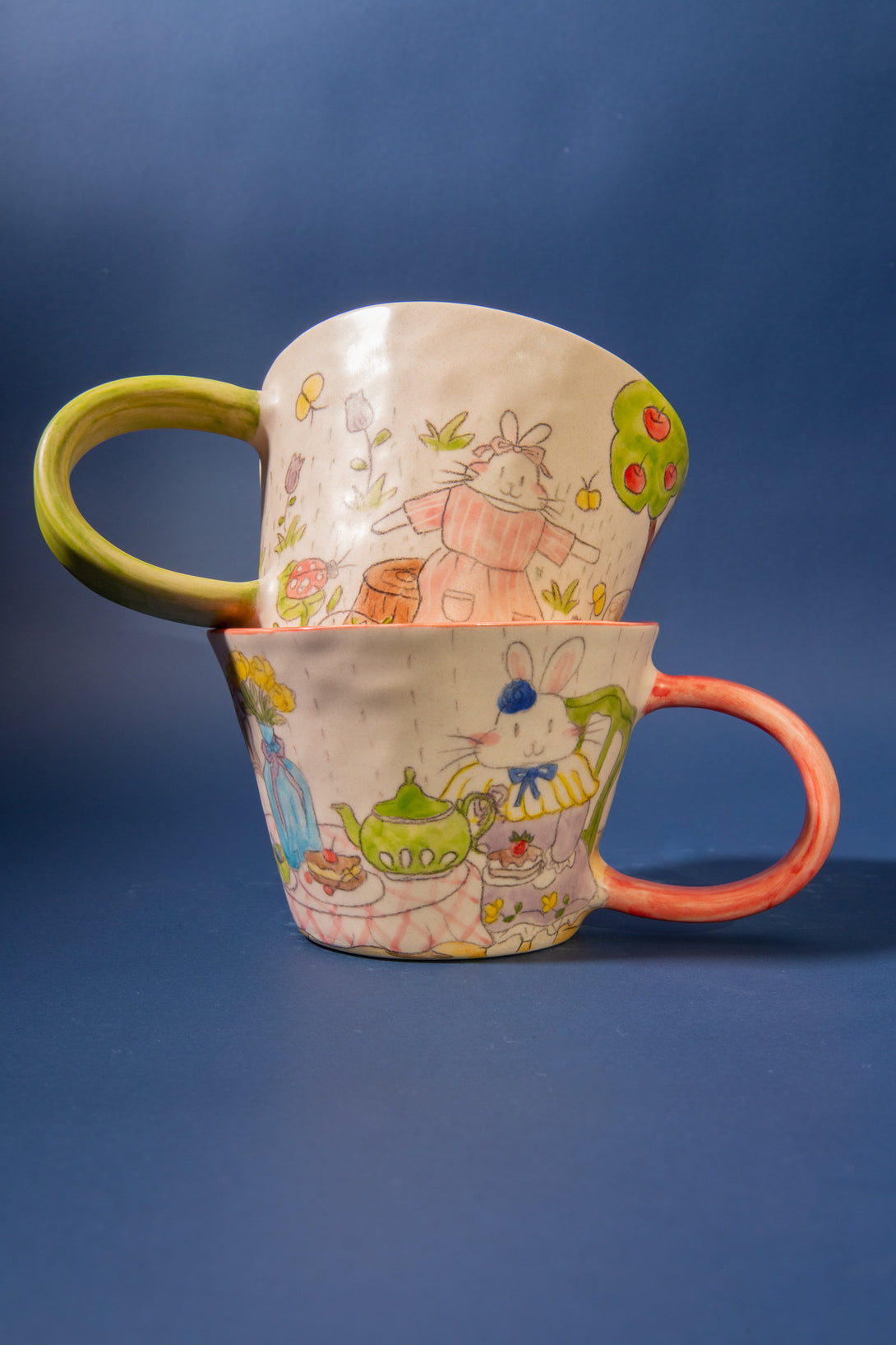 Two ceramic mugs with cartoon designs stacked on a blue background