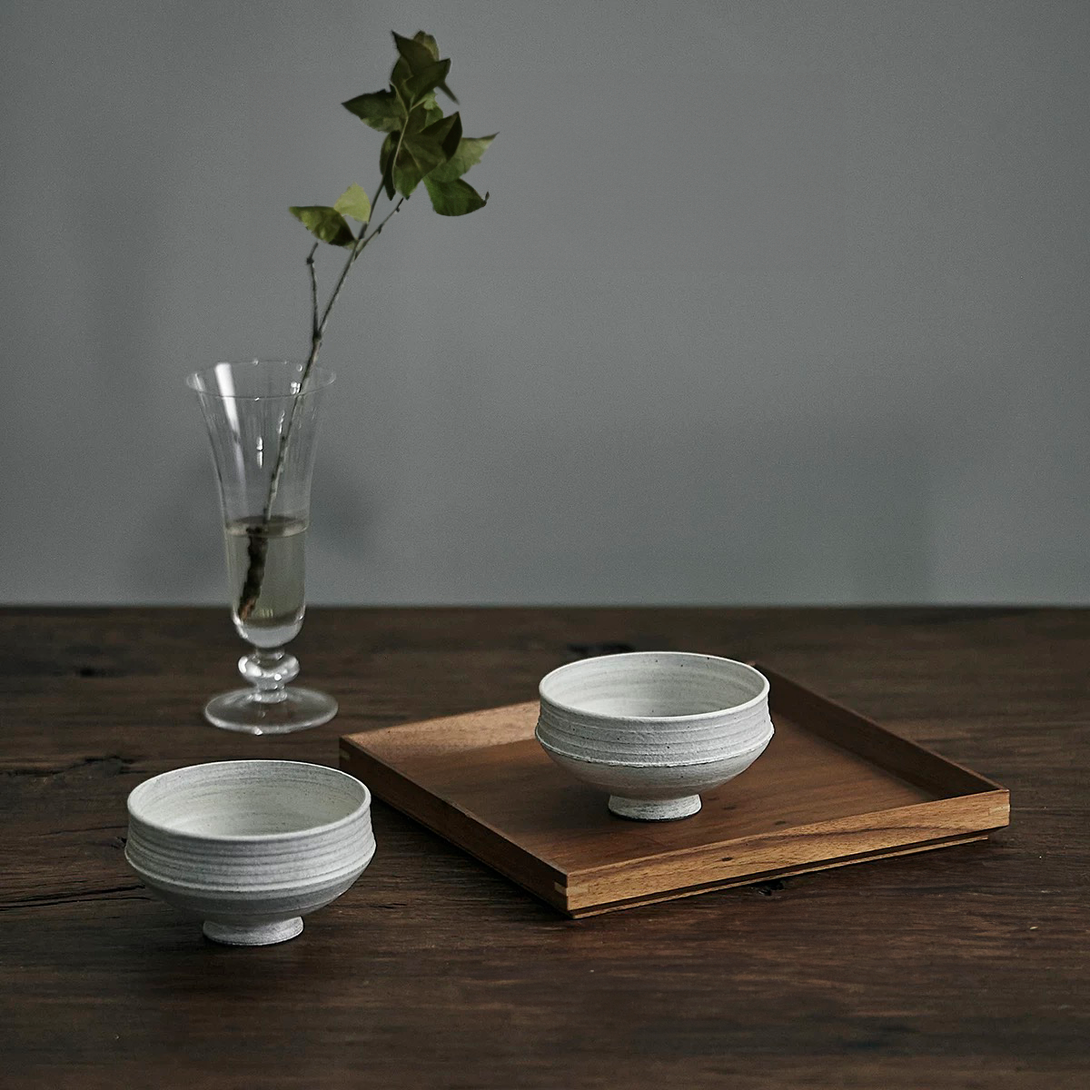 Two gray ceramic bowls with a simple design on a wooden tray