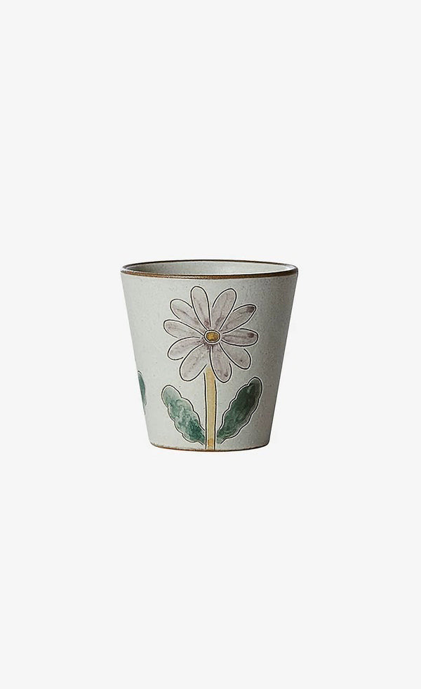 A ceramic cup with a floral pattern, featuring a large daisy flower in the center and leaves in the background.