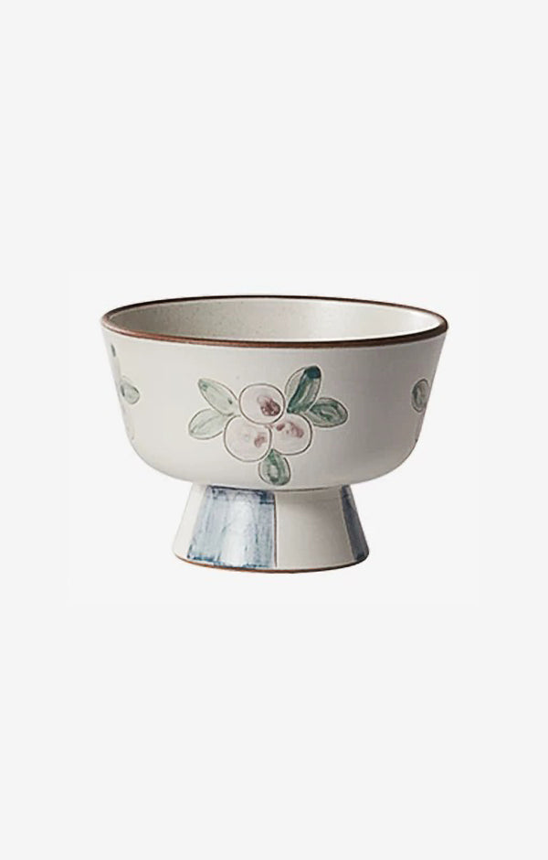 A white ceramic bowl with green and beige floral patterns and a blue foot ring.