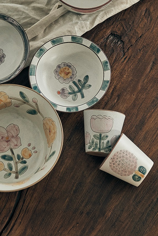 A ceramic cup with floral patterns in green and pink colors on a wooden background.