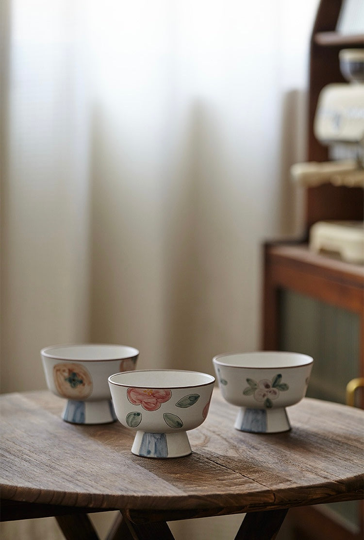 A white ceramic bowl with green and beige floral patterns and a blue foot ring.