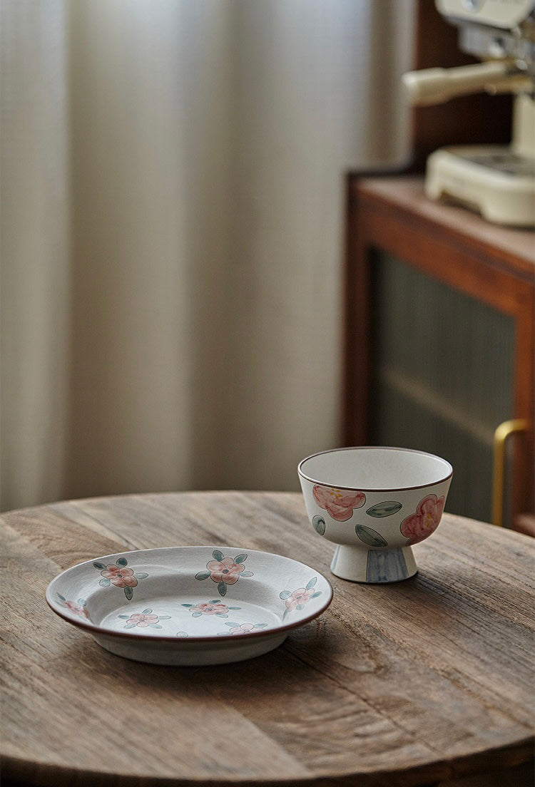 A white ceramic bowl with green and beige floral patterns and a blue foot ring.