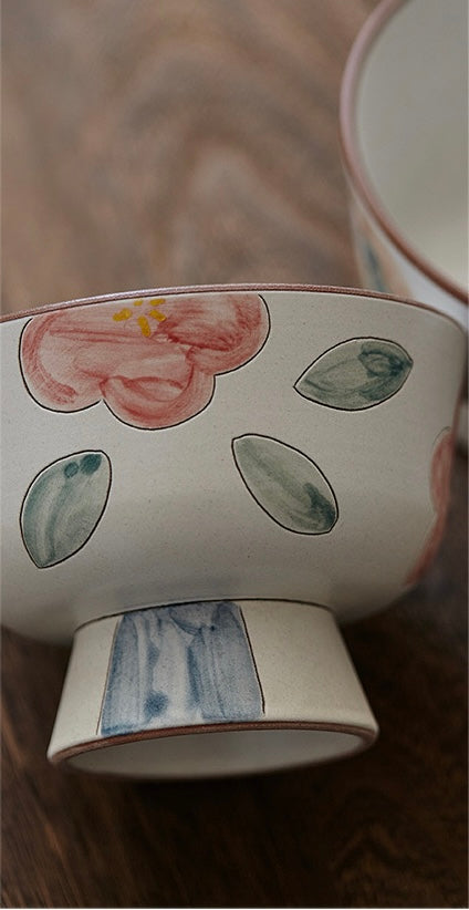 A white ceramic bowl with green and beige floral patterns and a blue foot ring.