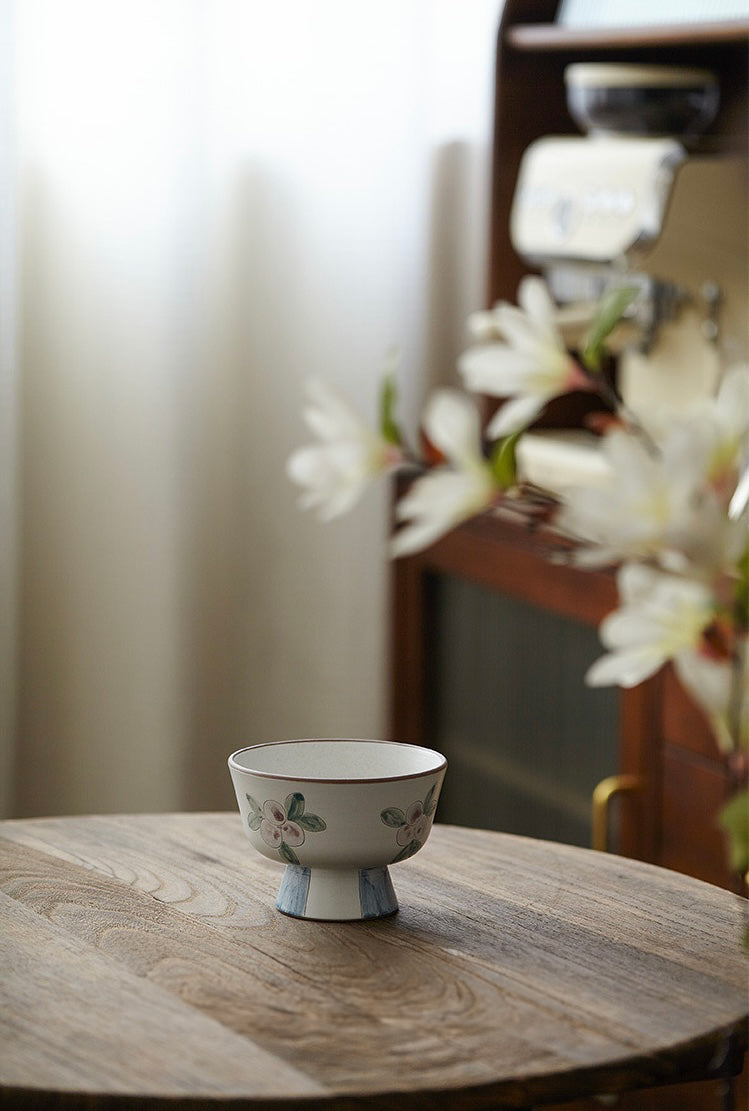 A white ceramic bowl with green and beige floral patterns and a blue foot ring.