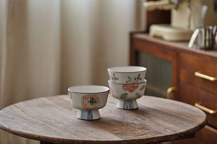 A white ceramic bowl with green and beige floral patterns and a blue foot ring.