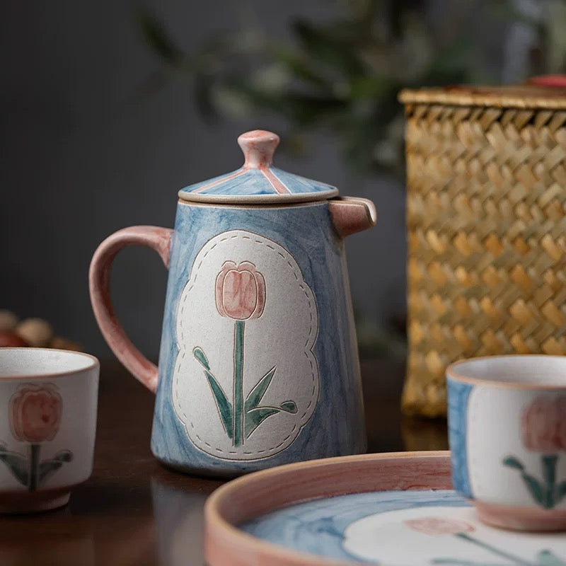 a set of teapot, cup and saucer in floral patterns, primarily in blue and pink colors.