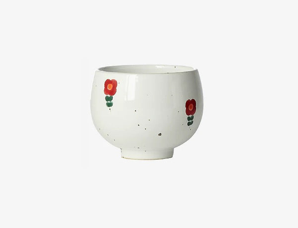 A white ceramic cup with red and green floral patterns on the side, displayed against a plain background.