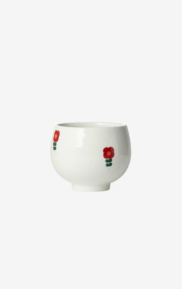 A white ceramic cup with red and green floral patterns on the side, displayed against a plain background.