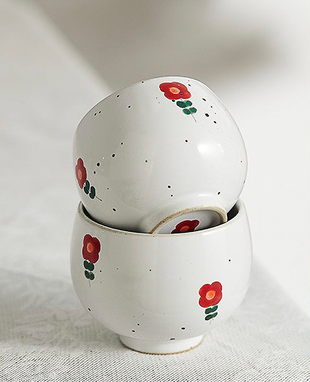 A white ceramic cup with red and green floral patterns on the side, displayed against a plain background.