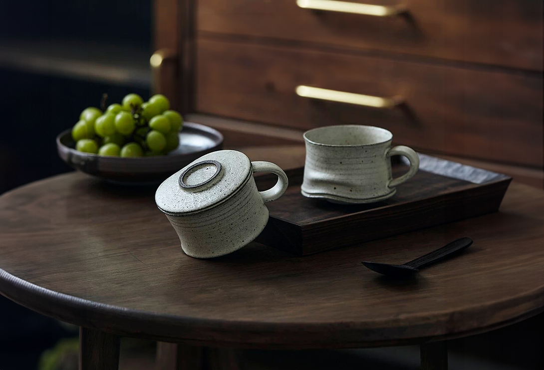 Two ceramic mugs on a wooden tray with grapes in the background