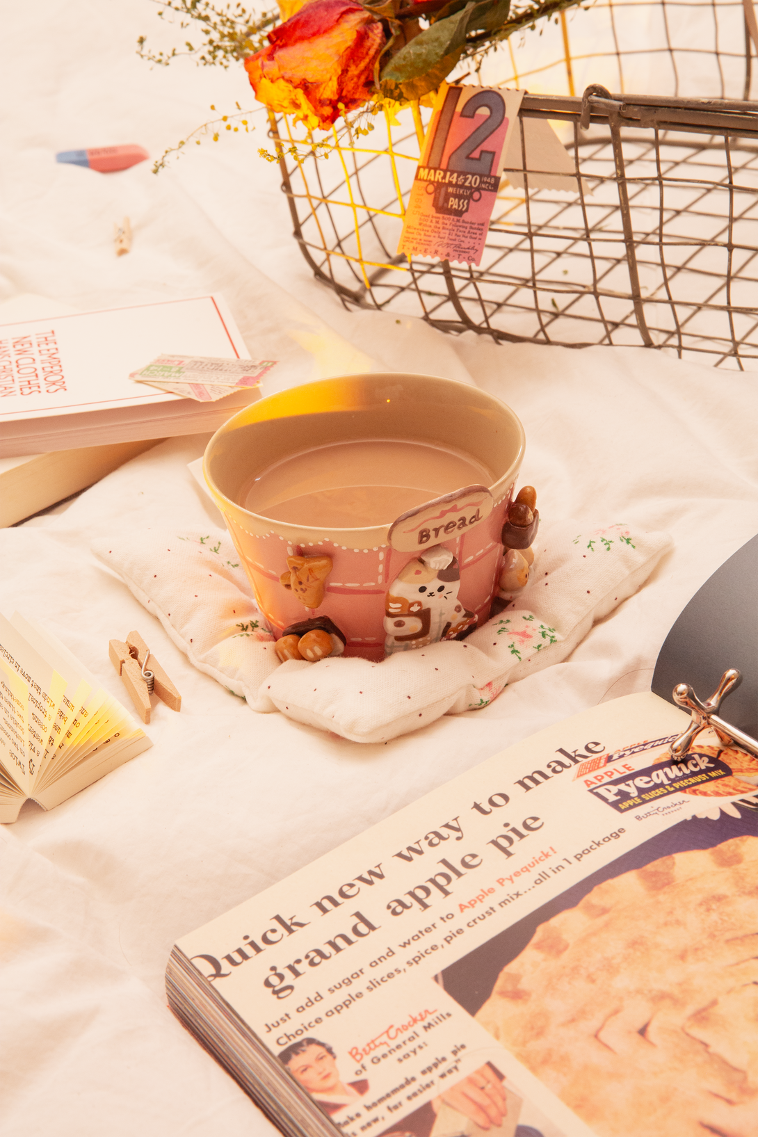 Pink Cup holding coffee on a book with a magazine and flowers in the background
