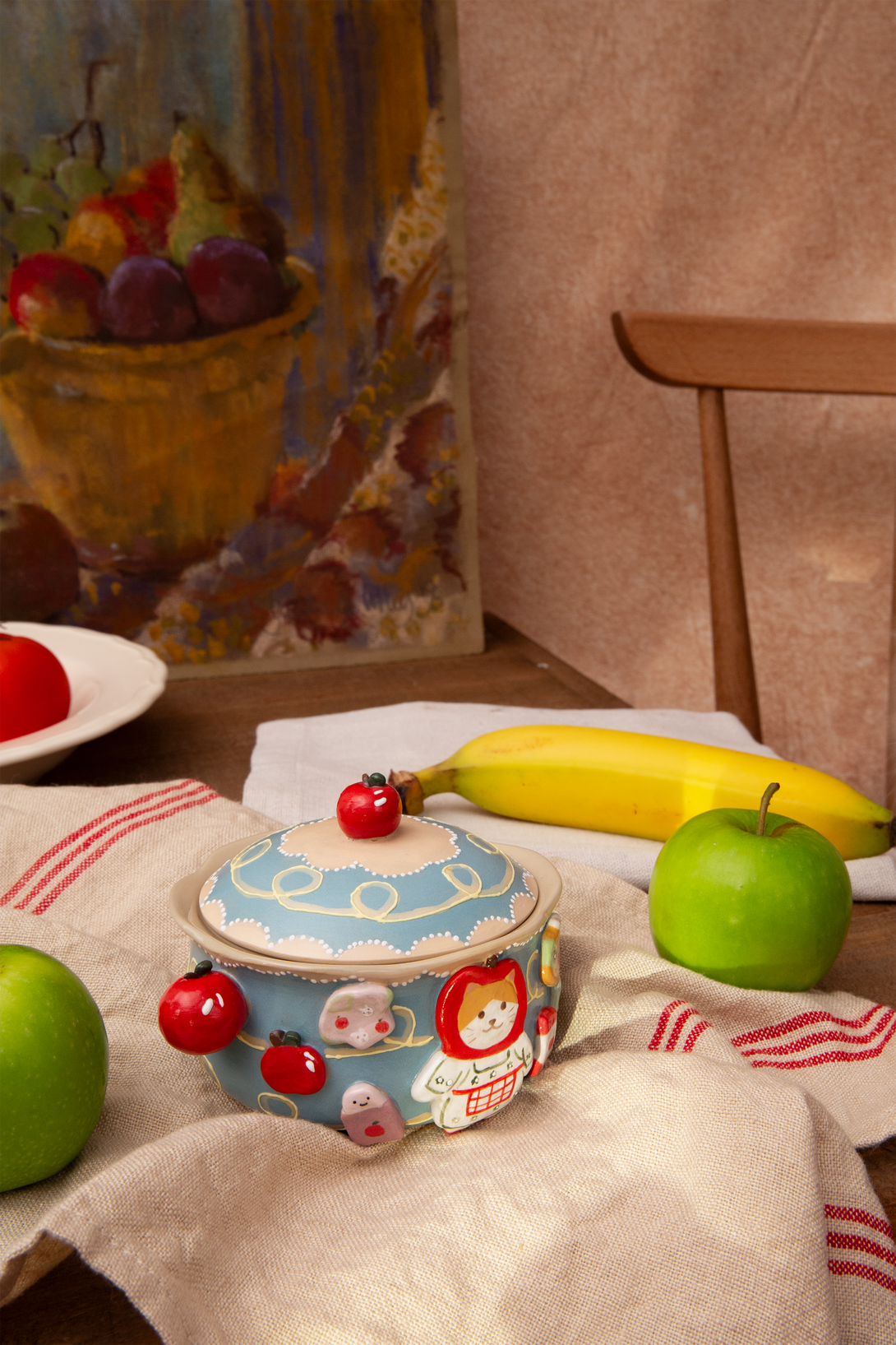 ceramic bowl with red elements on a table with fruits and a painting in the background
