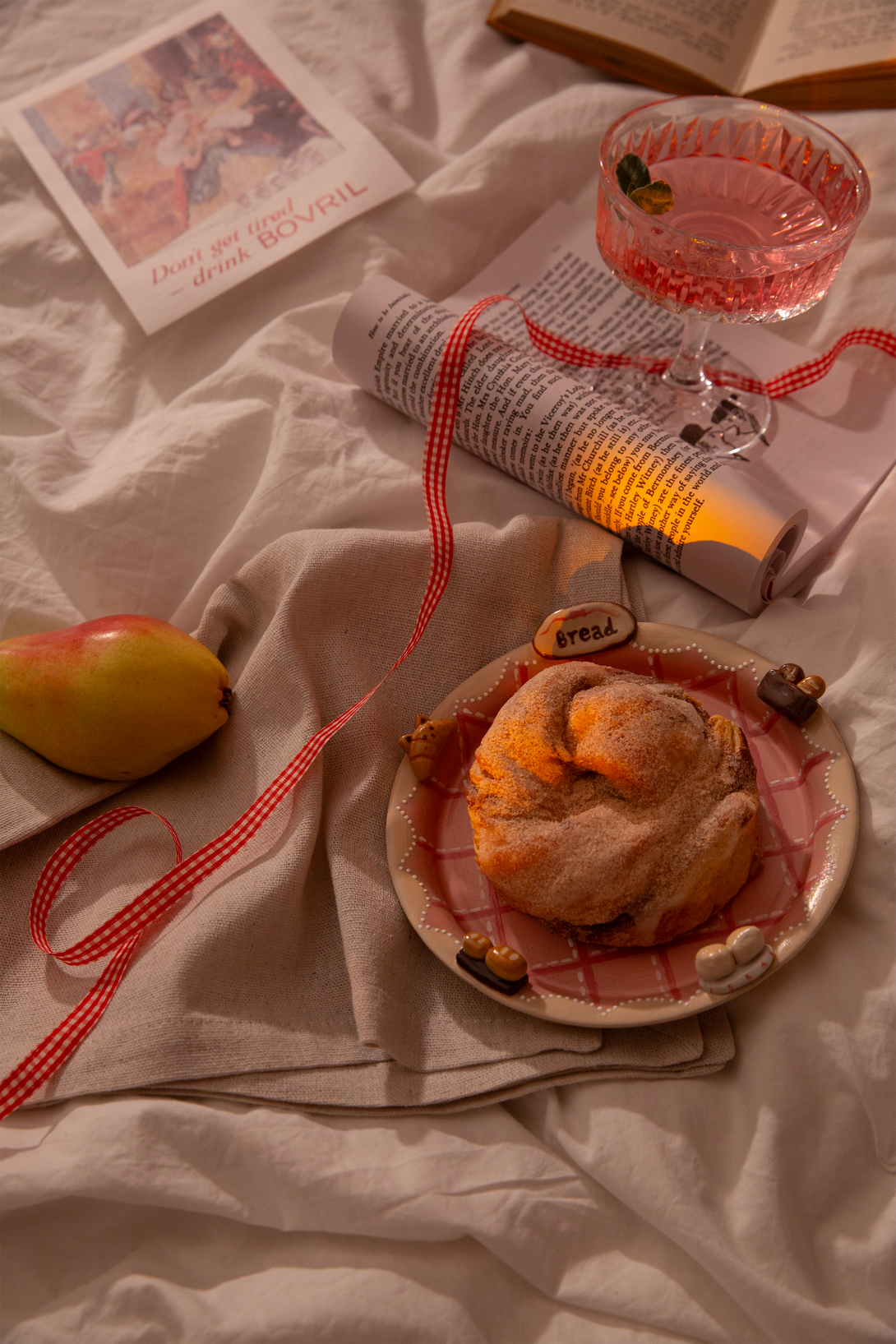 Cocktail glass with pink liquid, book, and pastry on pink ceramic serving plate on a white surface