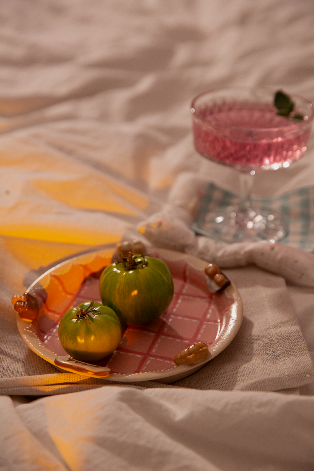 Two green fruits on a pink checkered plate with a glass of pink liquid in the background.