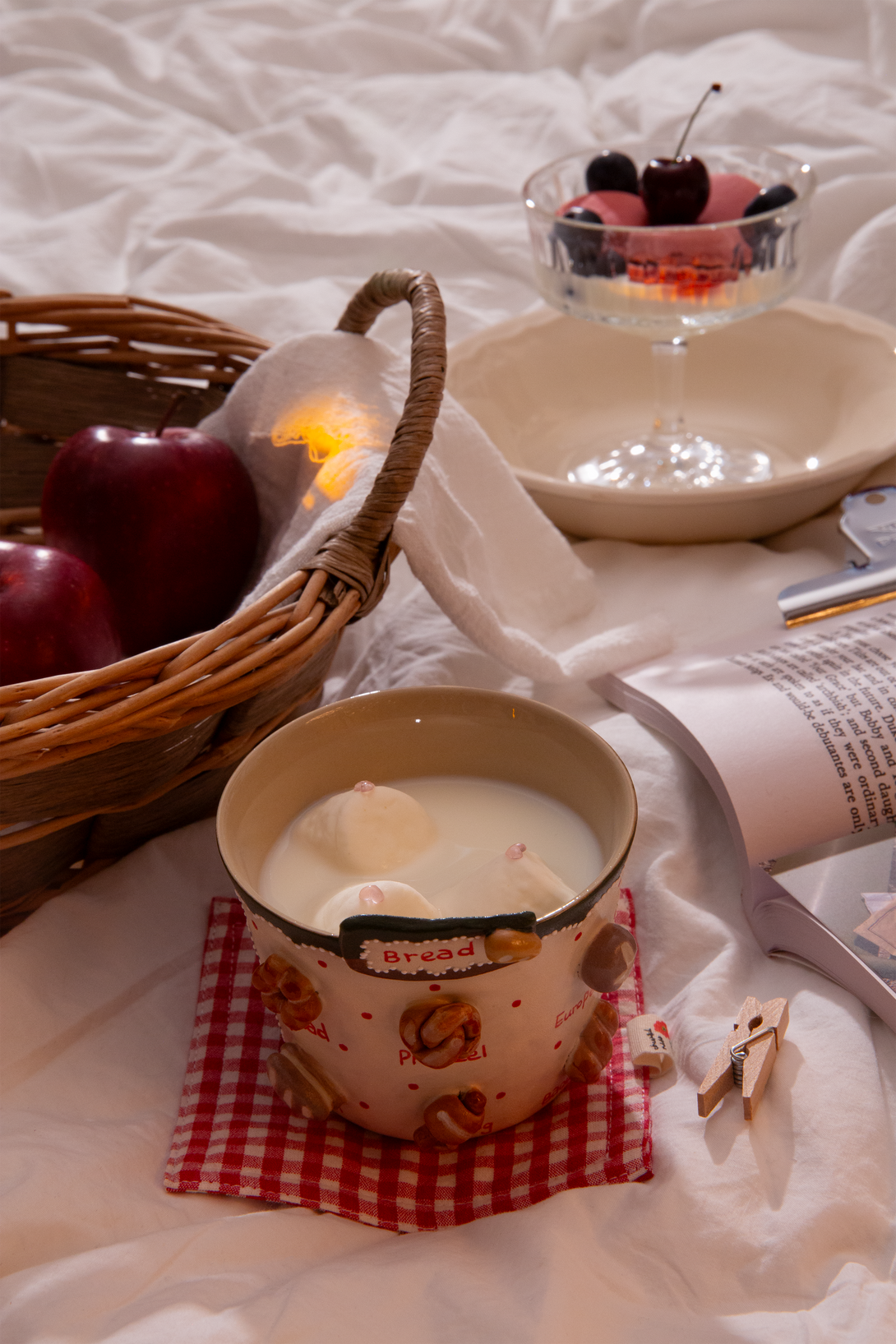Bread-themed handmade mug holding hot chocolate with marshmallows on a checkered cloth, surrounded by apples, a basket, and a bowl of cherries.