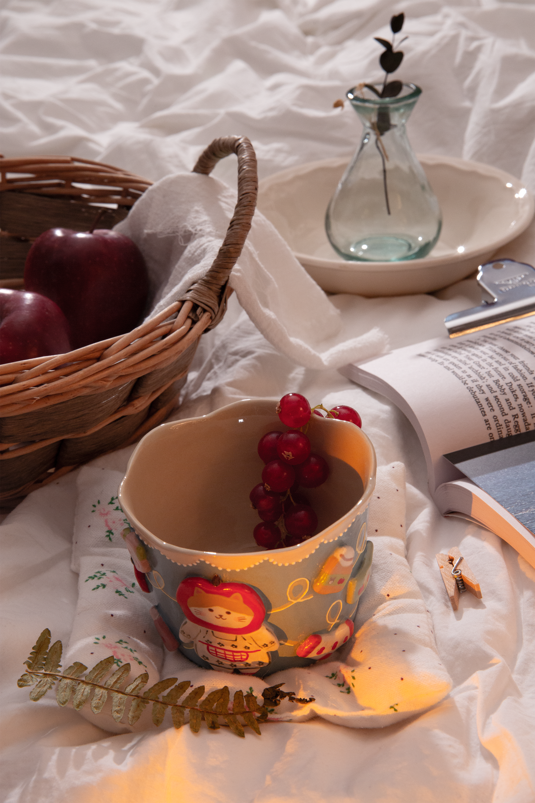 Cup with decorative design on a white surface with apples and a book.