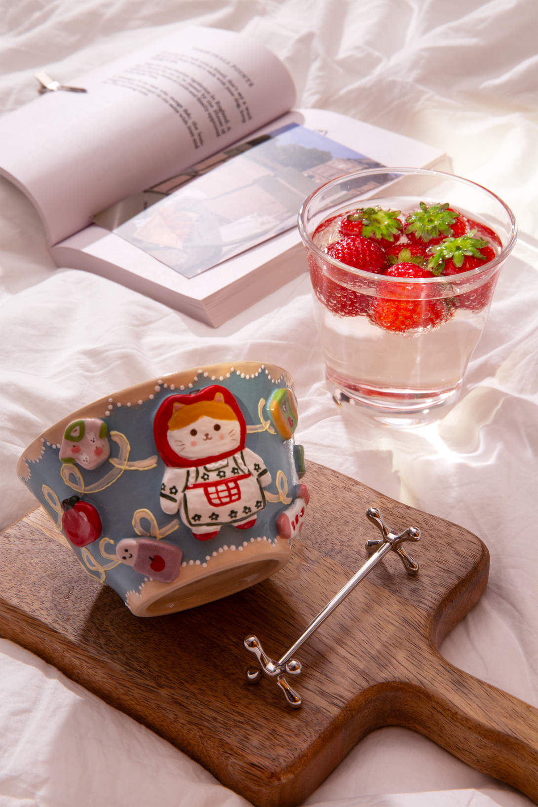 bowl with cartoon design on a wooden board, glass of strawberries, and book on a white surface