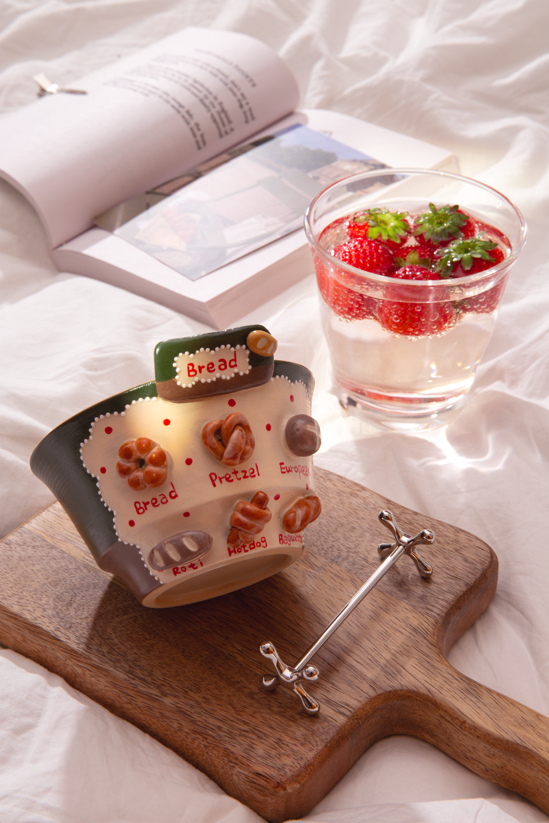 ceramic bowl with bread mptifs on a wooden board, next to a glass of water with strawberries.