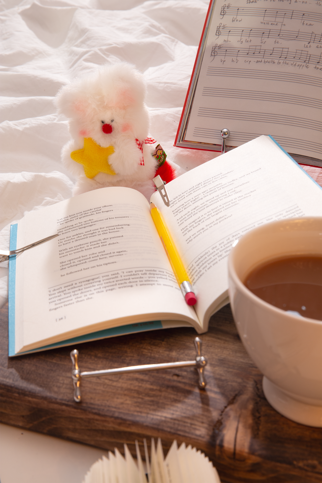 Open book with a pencil, cup of coffee, and small plush rabbit bag charm on a wooden surface.