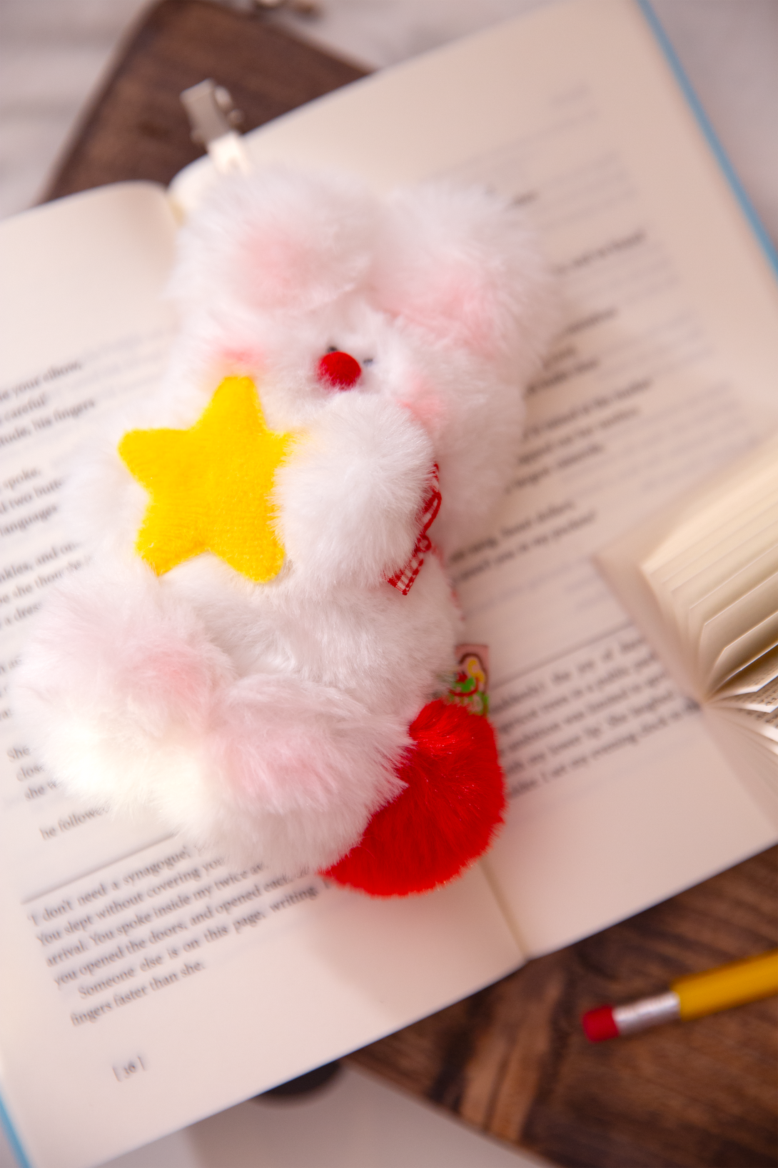 Plush bag charm with a star and red tail on an open book