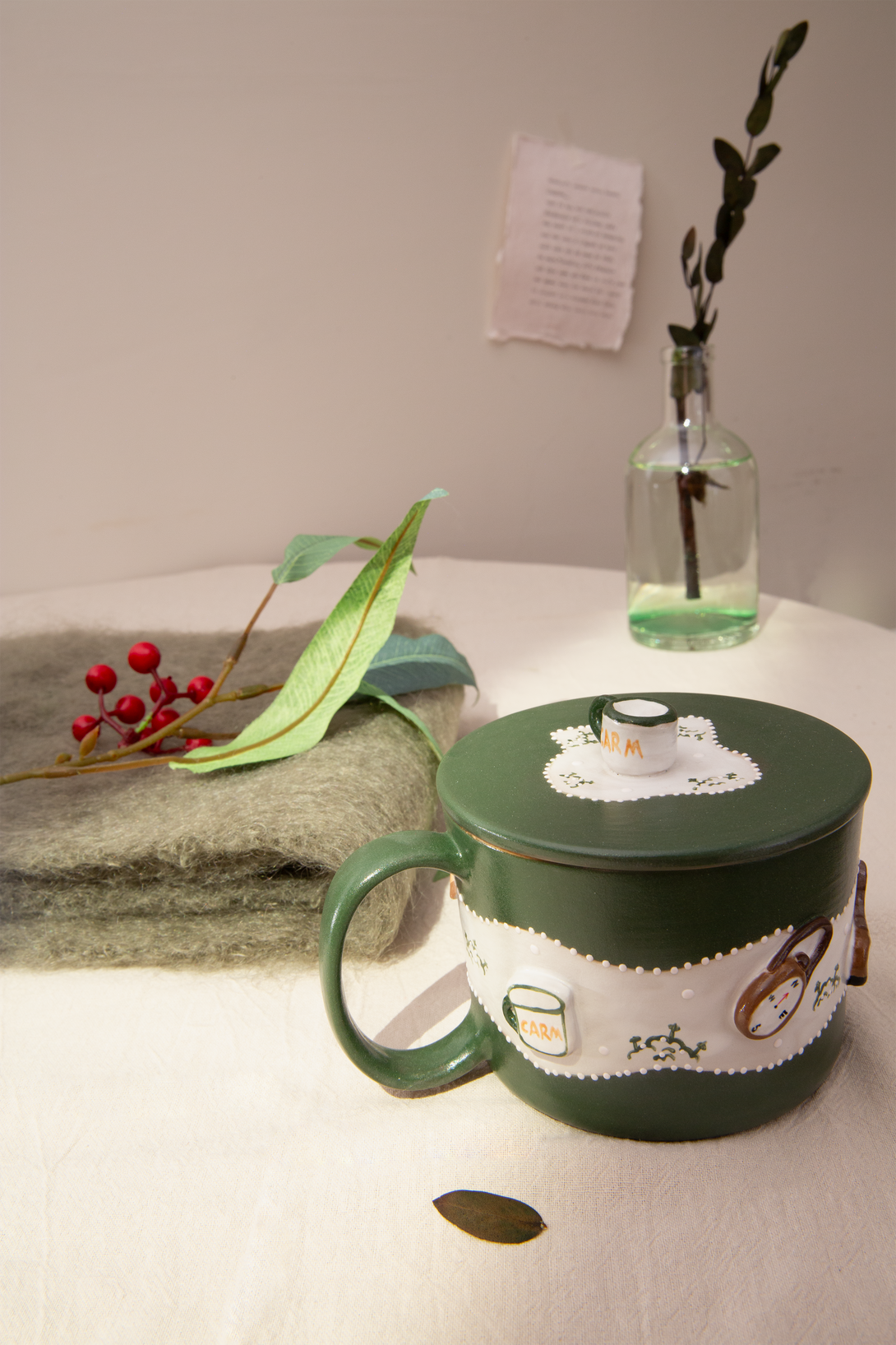 Green mug with decorative elements on a table with a vase and branches in the background