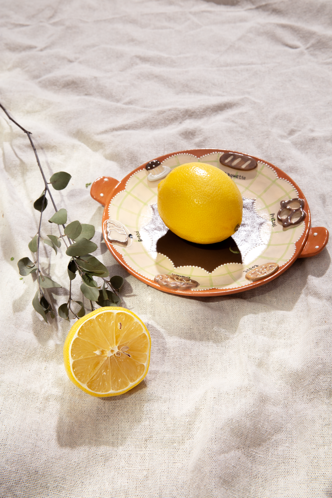 Two lemons on a ceramic handmade plate with a white fabric background