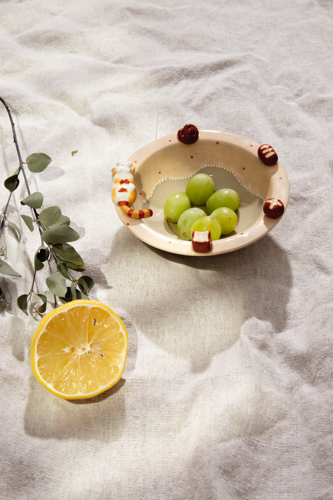 Small ceramic bowl with grapes on a textured surface with a lemon and leaves.