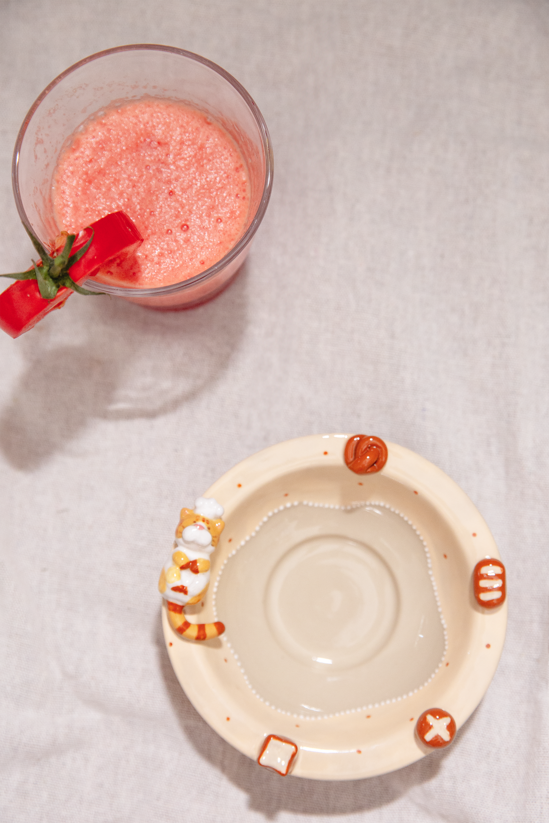 Pink smoothie in a glass with a straw next to a small ceramic bowl on a textured surface