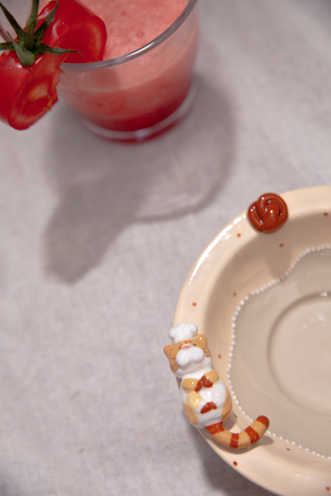 Small bowl with a cat design next to a glass of pink smoothie and tomatoes on a light gray surface.